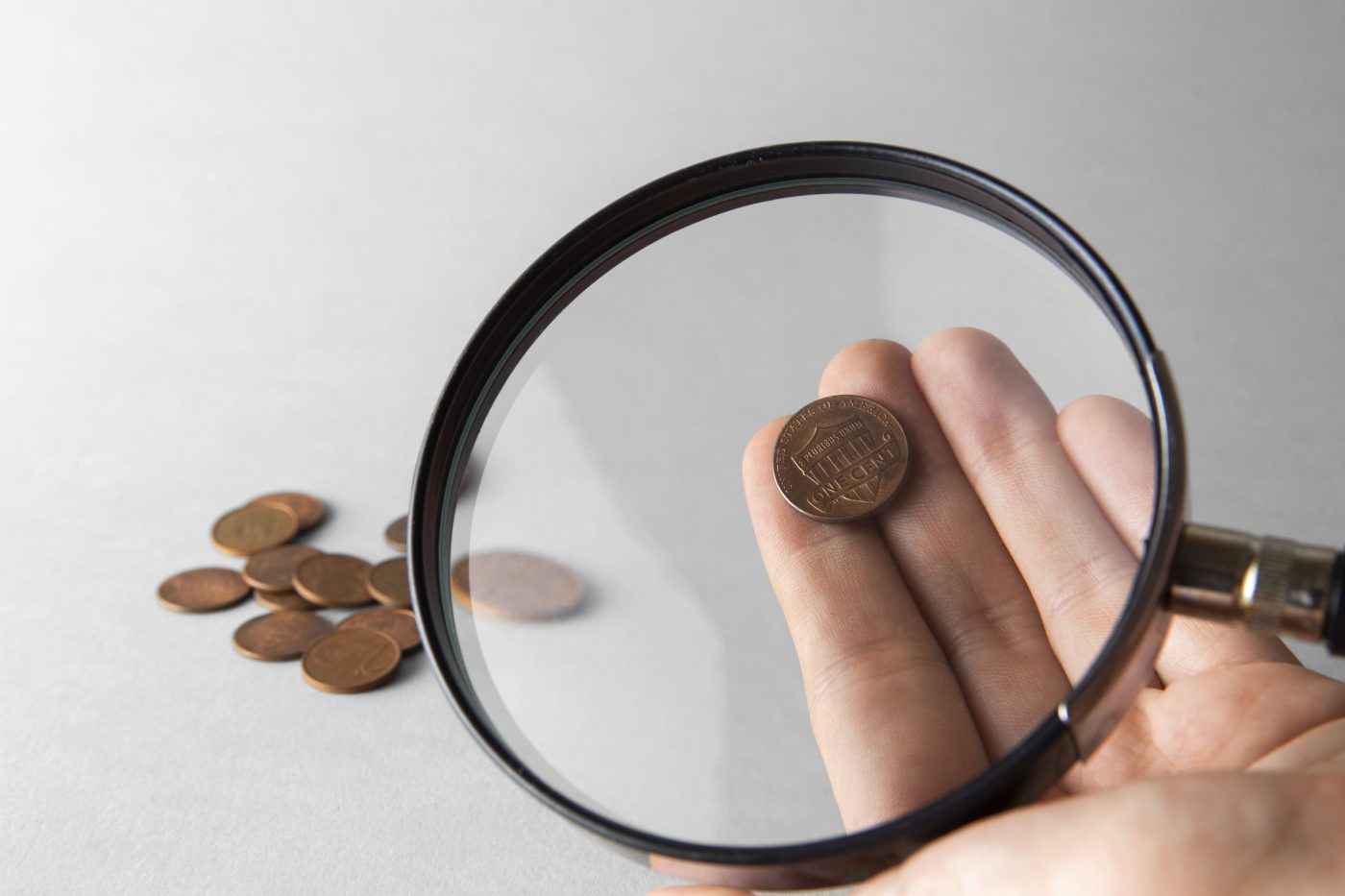 A magnifying glass held over a penny with more coins scattered nearby