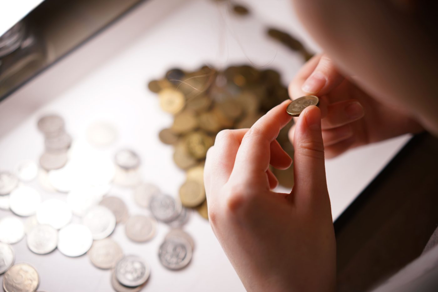 A person examining a coin over a spread of gold and silver coins